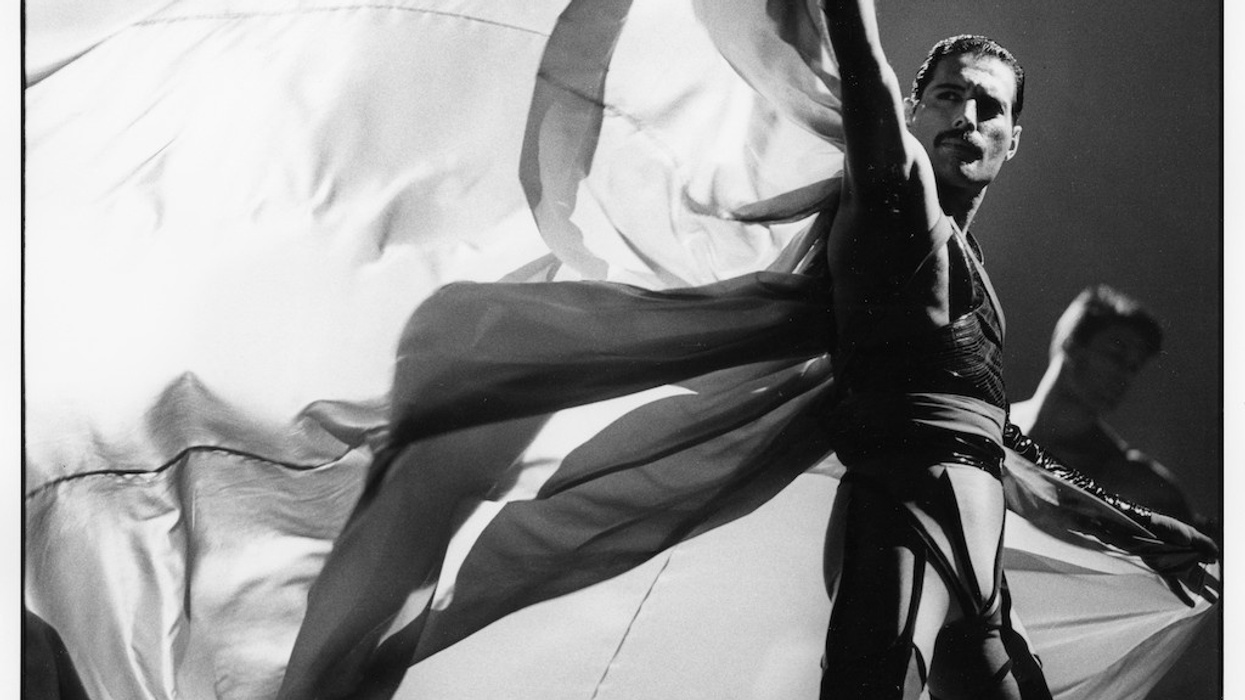 Freddie Mercury on stage with flowing fabric, striking a dramatic pose in black and white.