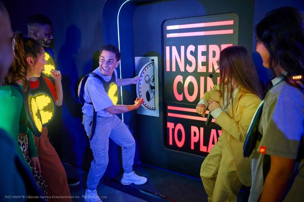 Friends in glowing gear react excitedly to an "Insert Coin to Play" sign in an arcade setting.
