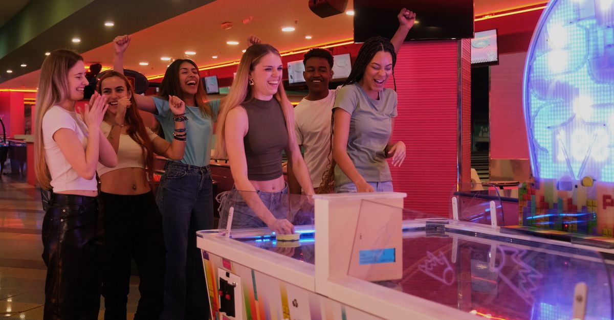 Friends playing air hockey at an arcade, cheering and smiling.