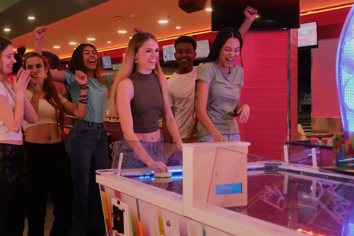 Friends playing air hockey at an arcade, cheering and smiling.