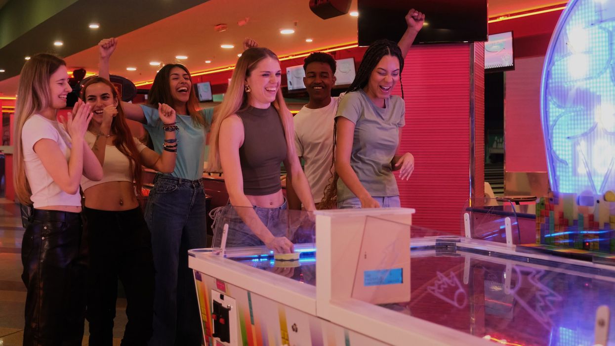 Friends playing air hockey at an arcade, cheering and smiling.