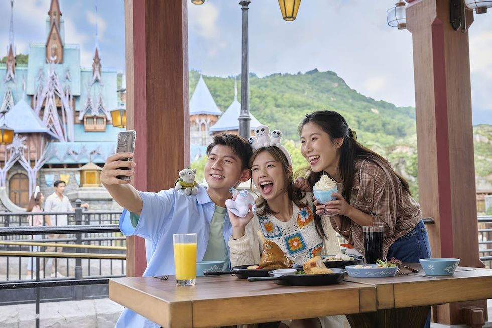 Friends take a selfie at Hong Kong Disneyland, with food and a castle in the background.