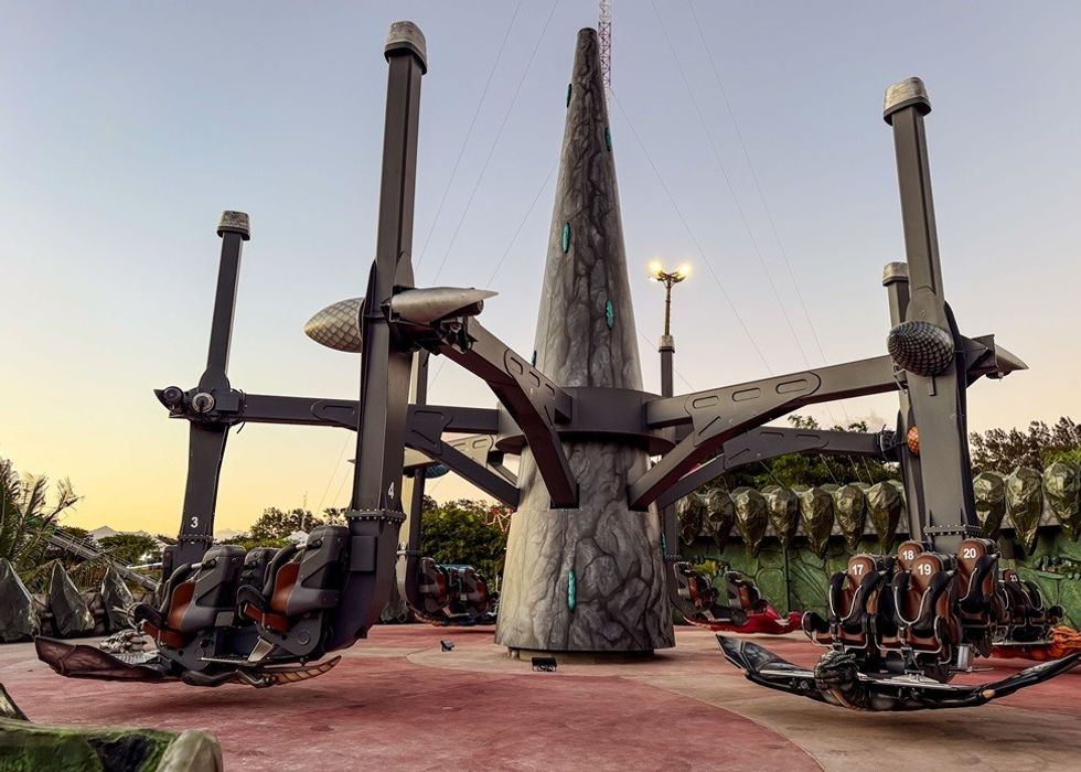 Futuristic amusement park ride with rotating arms and suspended seats at sunset.