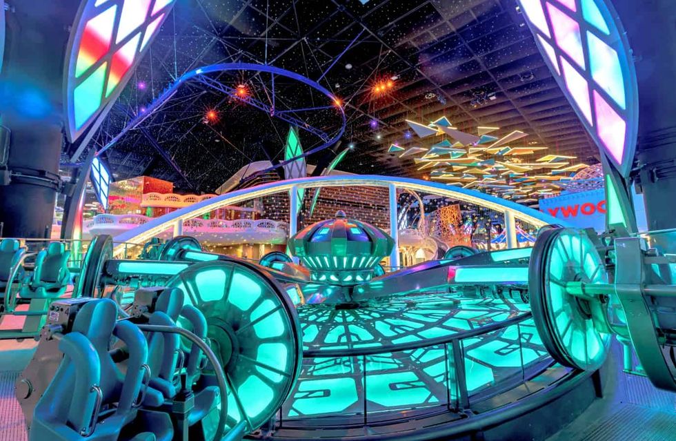 Futuristic amusement park ride with vibrant neon lights and a starry ceiling at Quest