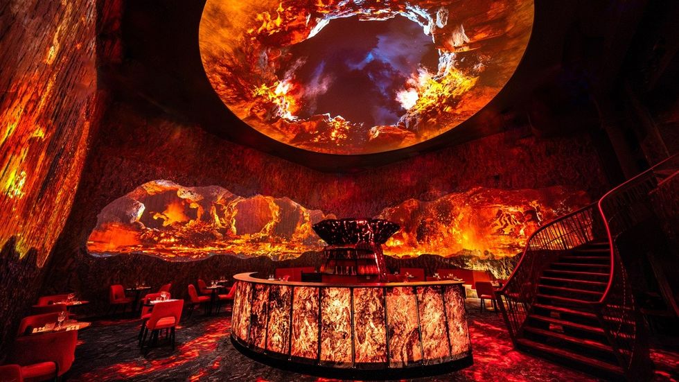 Futuristic bar with fiery, immersive wall and ceiling displays resembling lava.