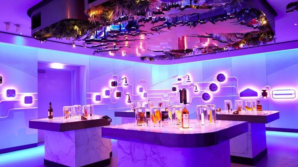 Futuristic bar with neon lights, white marble counters, and colorful bottles on display.