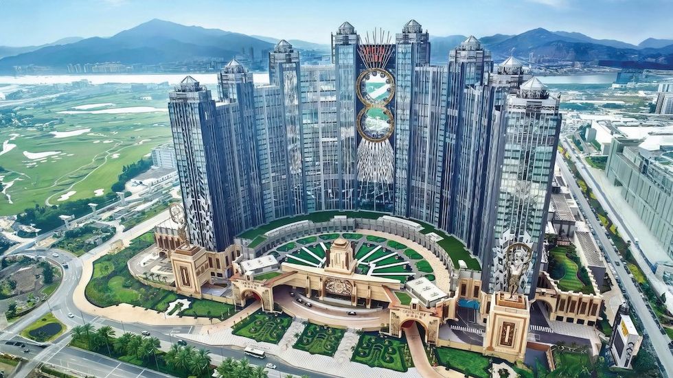 Futuristic building with glass towers and circular design, set in a lush landscape and mountains.