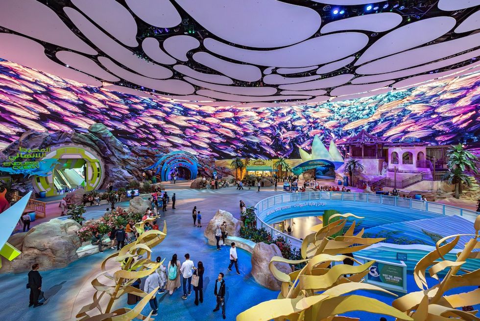 Futuristic, colorful theme park with digital sea effects on the ceiling and diverse visitors below SeaWorld Abu Dhabi