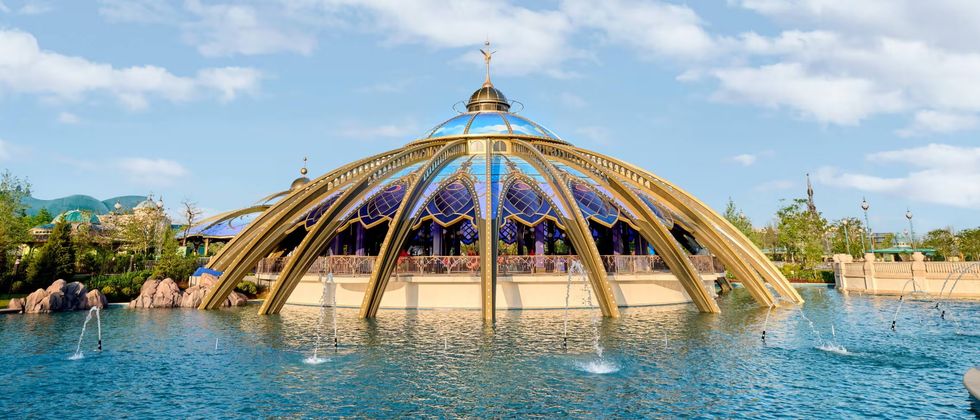 Futuristic dome structure with golden arches over water, surrounded by fountains and greenery.