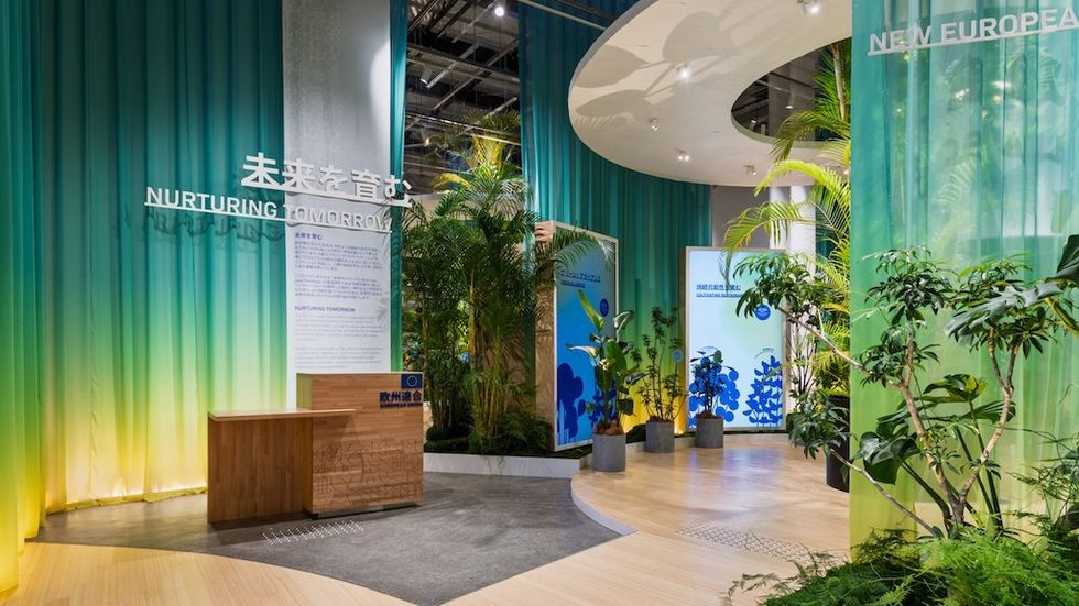 Futuristic exhibit with green plants and signage reading "Nurturing Tomorrow" in various languages.