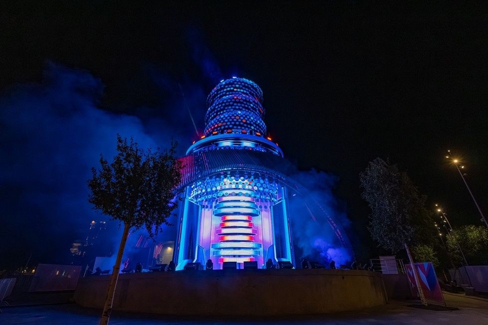 Futuristic, illuminated tower with vibrant blue and red lights against a night sky.