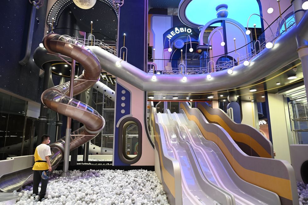 Futuristic indoor playground with slides and ball pit, under a glowing blue ceiling.