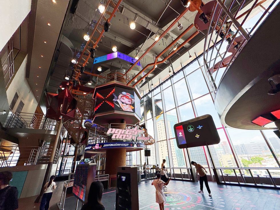 Futuristic indoor space with screens, high ceiling, and large windows; people exploring.