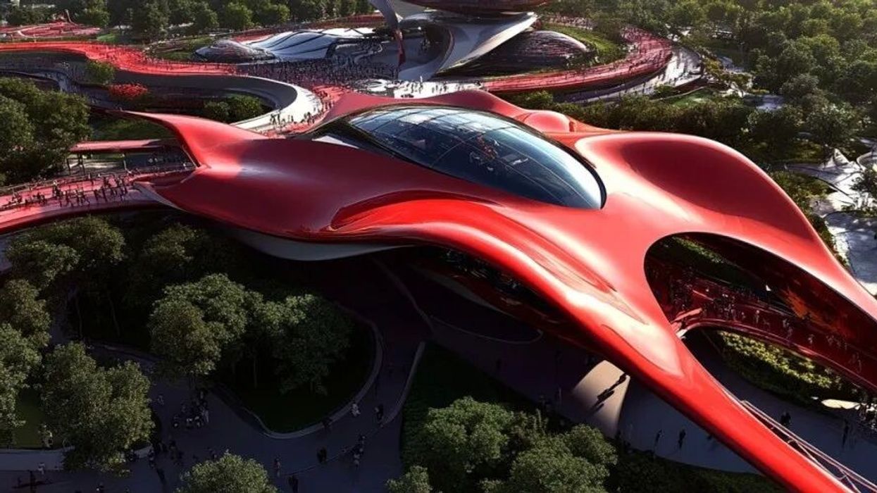 Futuristic red building with sleek curves and glass dome surrounded by green trees.