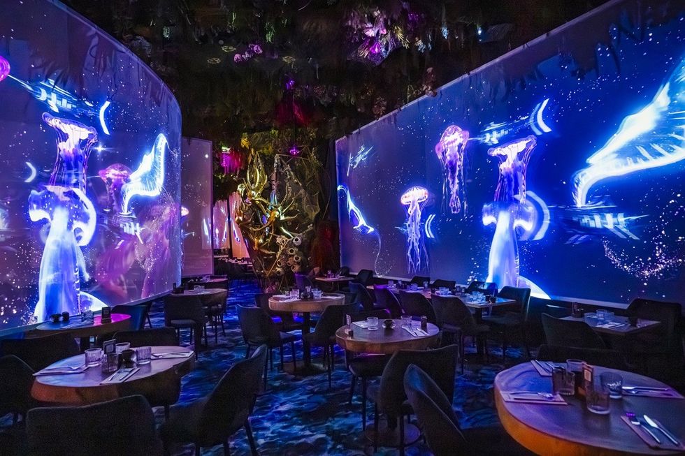 Futuristic restaurant with glowing jellyfish projections on walls.