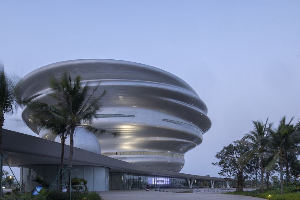 Futuristic round building called the Hainan Science Museum with palm trees under a clear sky.