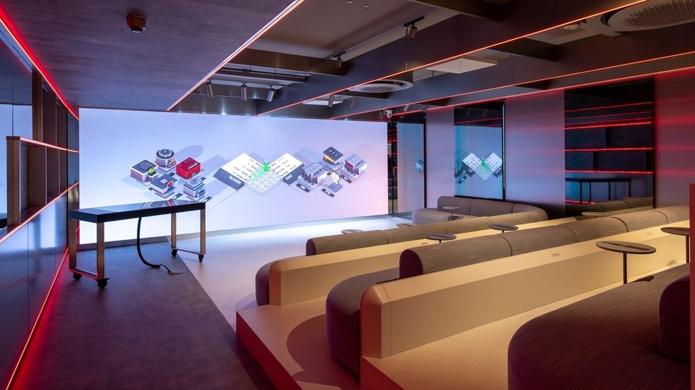 Futuristic seating area with a large digital display on the wall, lit by red neon accents at Coca-Cola's customer experience centre, THE 6TH FLOOR