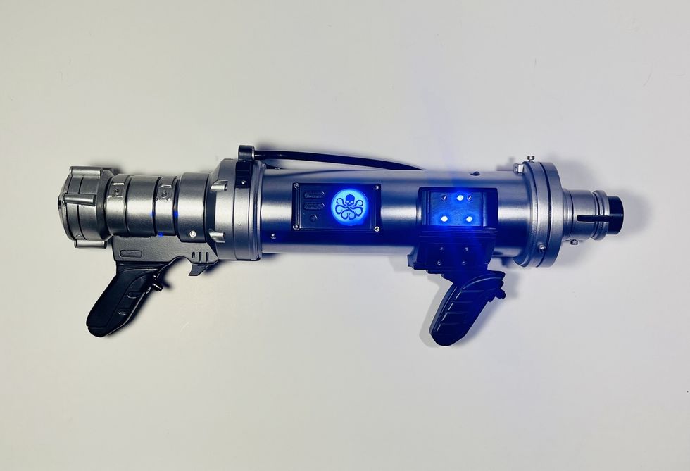 Futuristic silver prop gun with blue glowing lights and black handles.