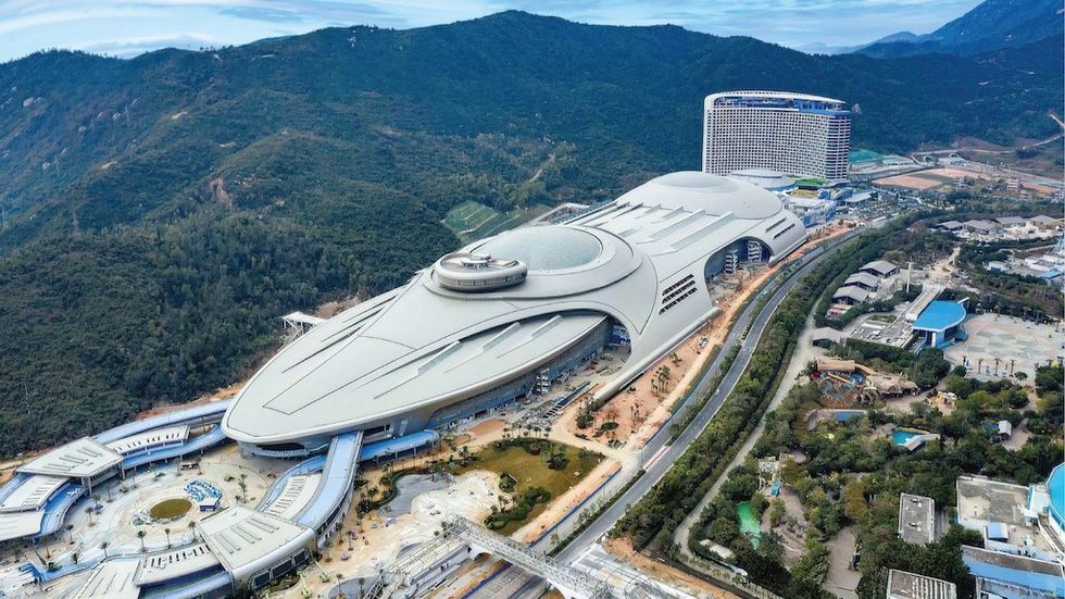 Futuristic spaceship-like building amid green mountains and winding roads.