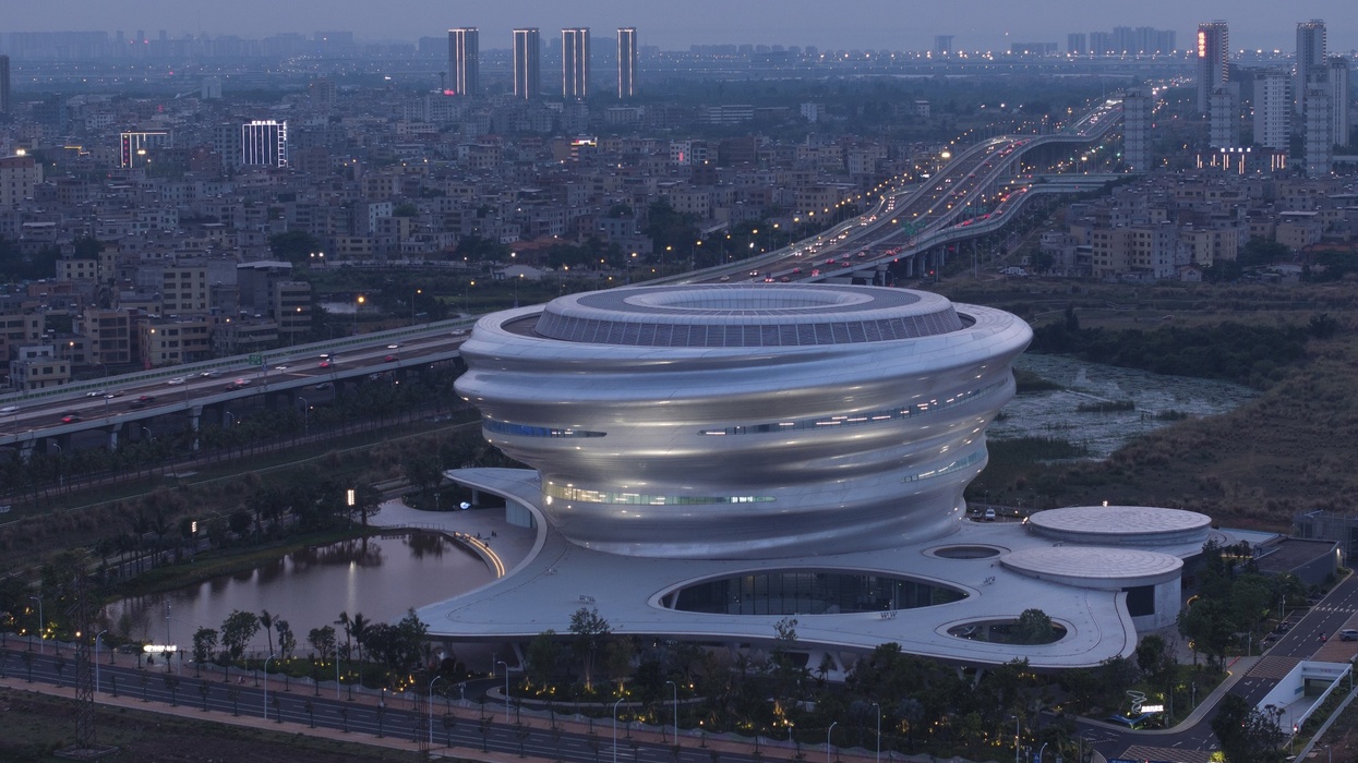 Futuristic spiral building called the Hainan Science Museum in a cityscape during dusk, with roads and lights visible.