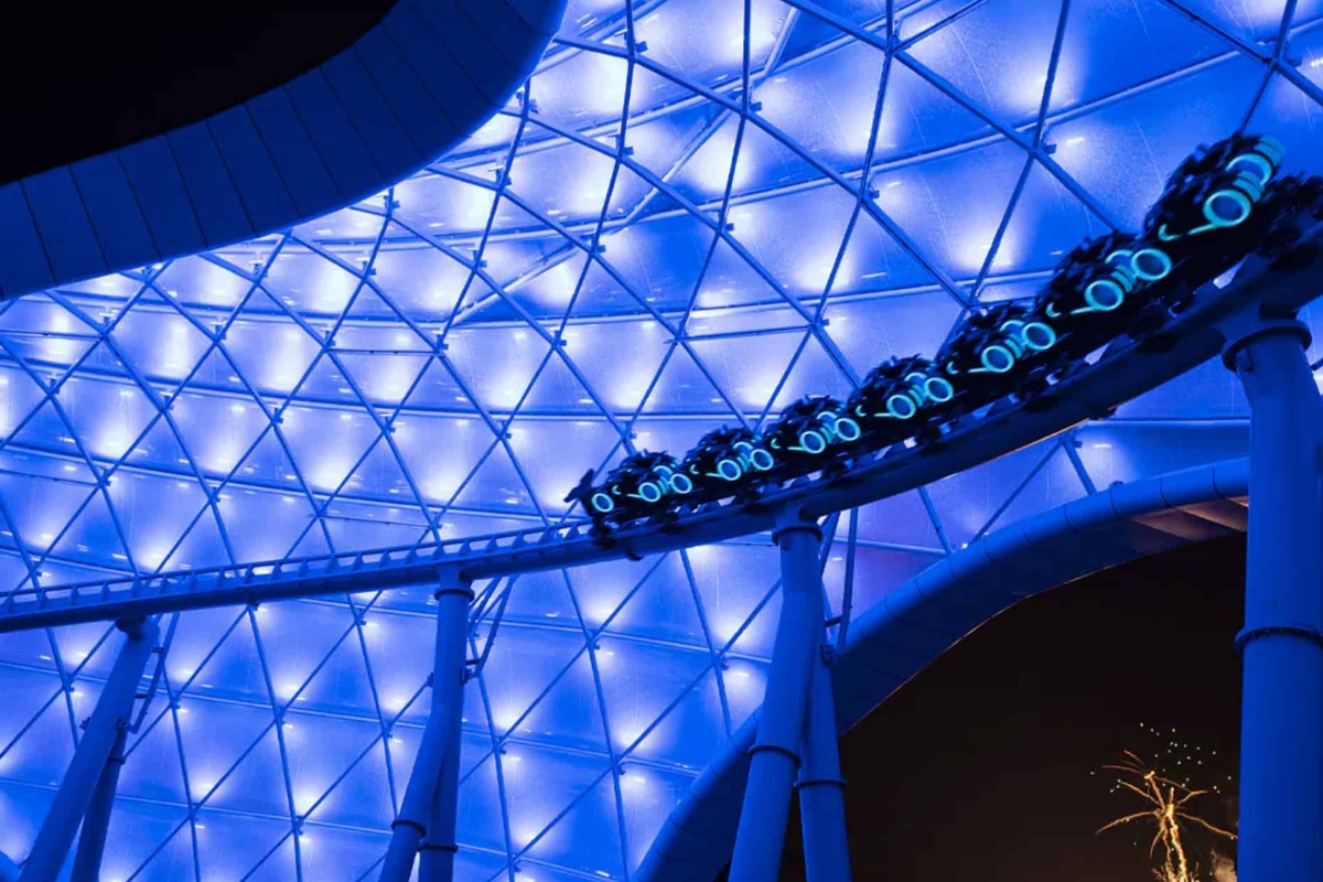 Futuristic Tron roller coaster under glowing blue lights at night.