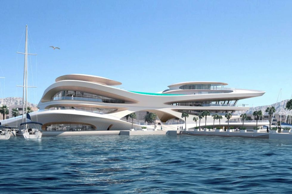 Futuristic waterfront building with curved design, boats, and palm trees under clear blue sky at Amaala