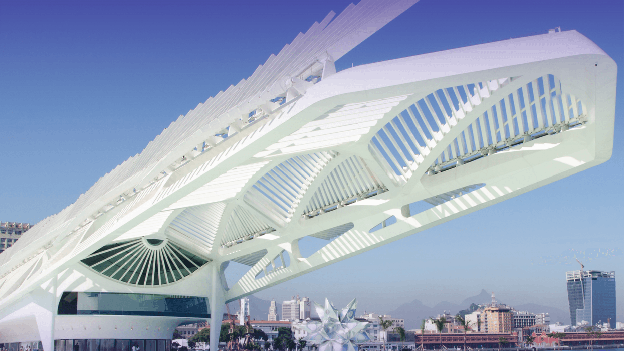 Futuristic white building with geometric design against a clear blue sky, near a waterfront.