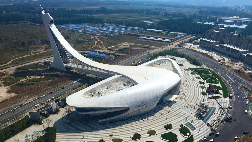 Futuristic white building with sweeping curves and a tall, arching structure in a modern landscape.