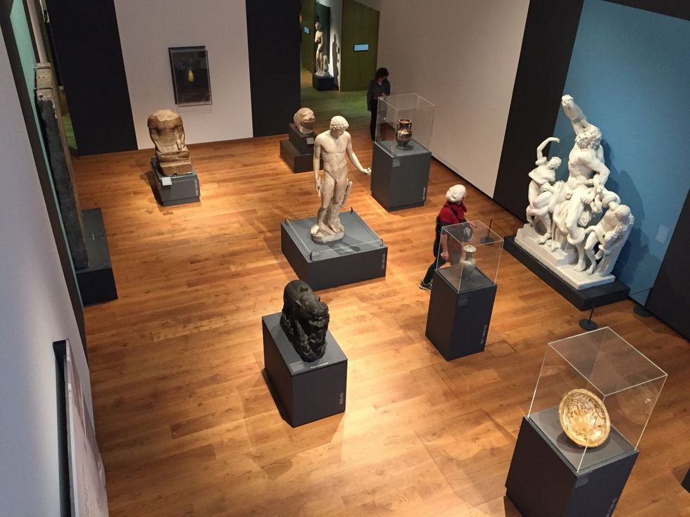 Gallery at the Ashmolean Museum of Art and Archaeology, with classical sculptures and visitors on wood flooring.