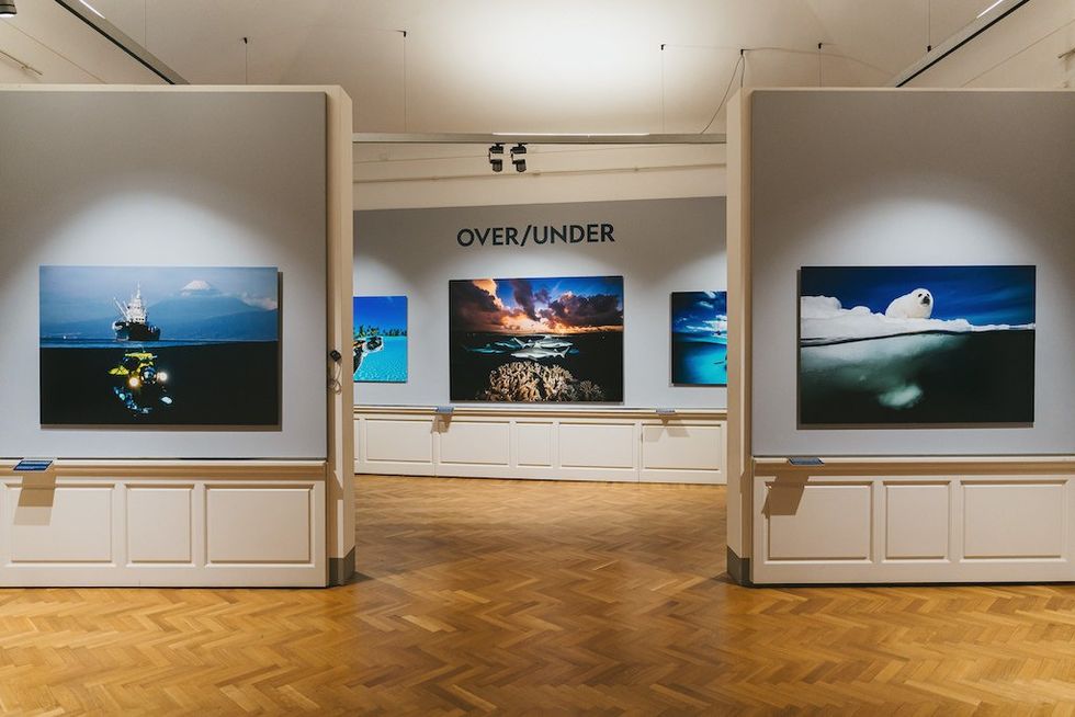 Gallery with ocean-themed photos under "Over/Under" sign on the wall.