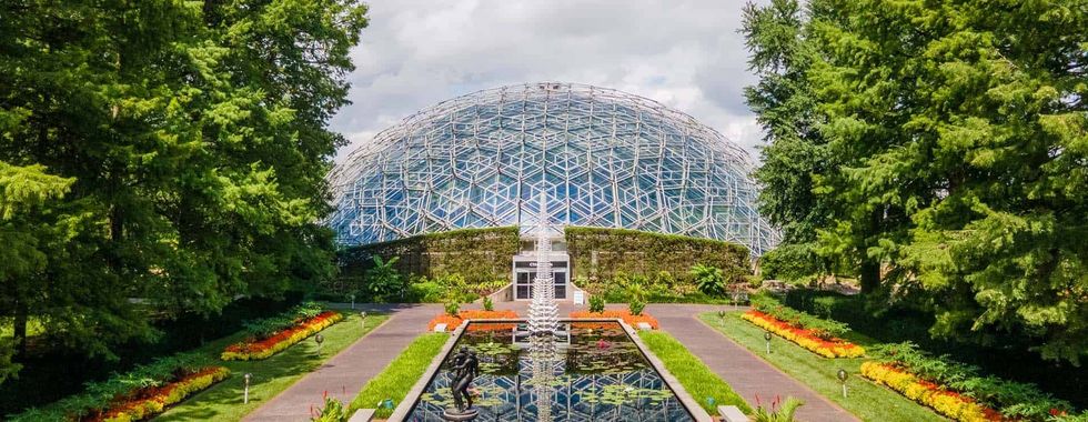 Geodesic dome greenhouse at Missouri Botanical Garden with a reflecting pond and colorful gardens in the foreground.