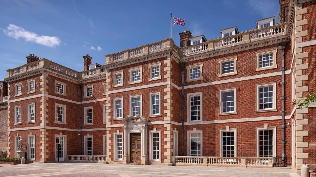 Georgian-style red brick mansion called Trent Park House of Secrets with UK flag under a clear blue sky.