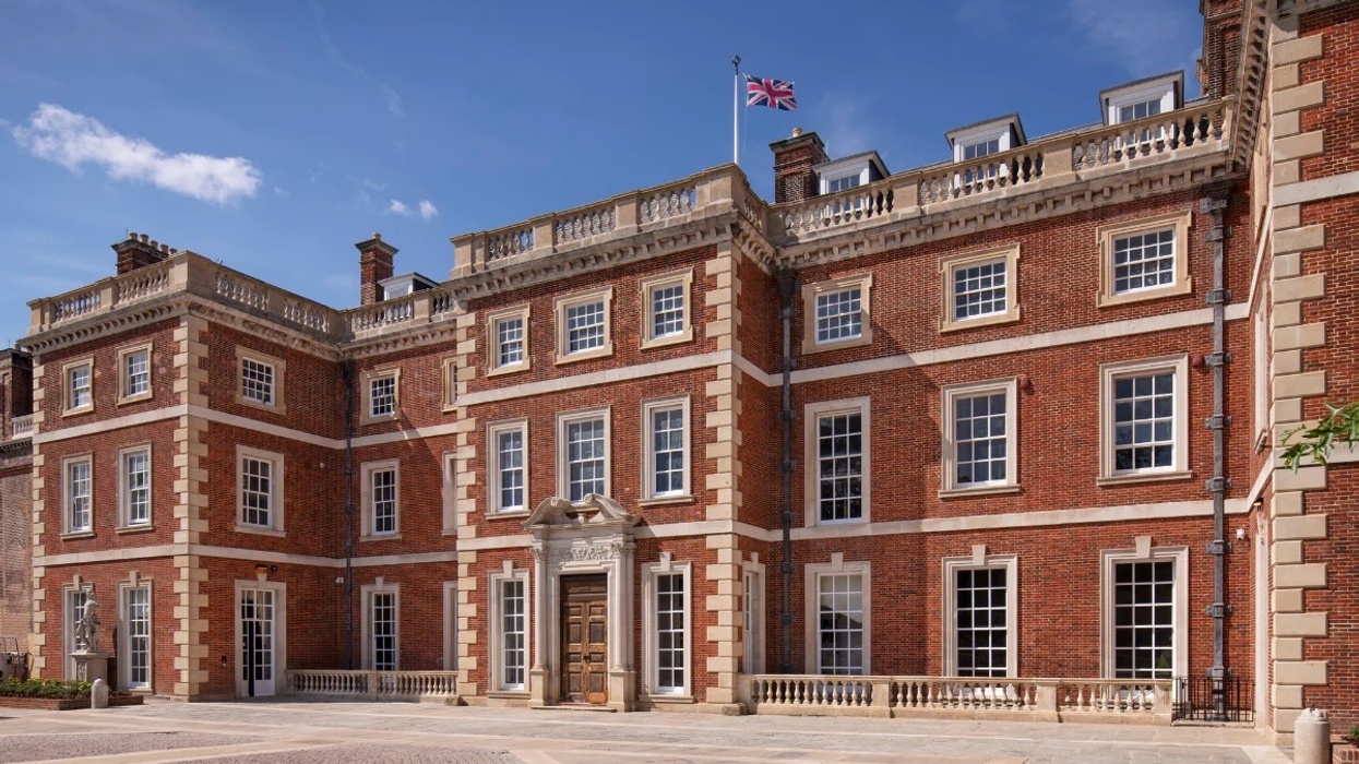 Georgian-style red brick mansion called Trent Park House of Secrets with UK flag under a clear blue sky.