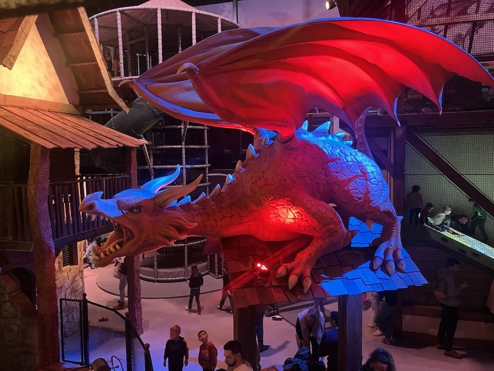 Giant dragon sculpture lit in red and blue, inside BillyBird Drakenrijk indoor play area with people below.