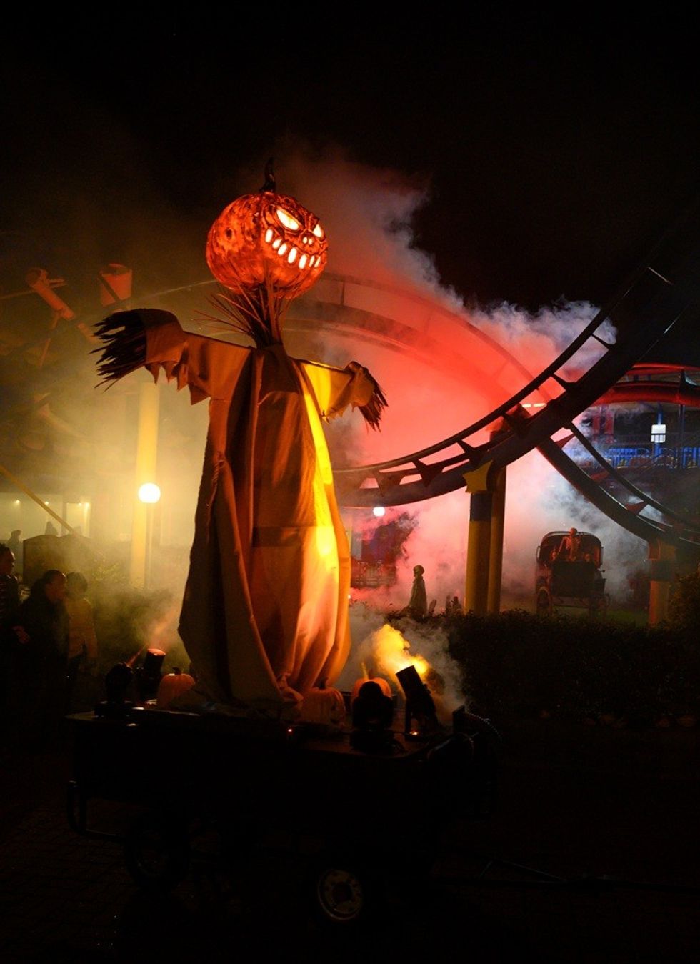 Giant jack-o'-lantern scarecrow illuminated in foggy, eerie fairground at night.