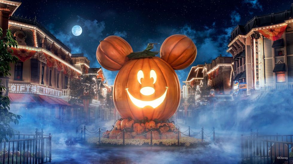 Giant Mickey-shaped pumpkin glowing on a foggy, moonlit Main Street decorated for Halloween.