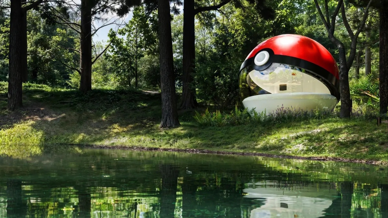 Giant Poké Ball structure in a forest, reflected in a tranquil pond.
