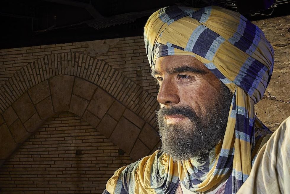 Giant sculpure of man in striped turban and robe against a stone arched background at Alif \u2013 The Mobility Pavilion