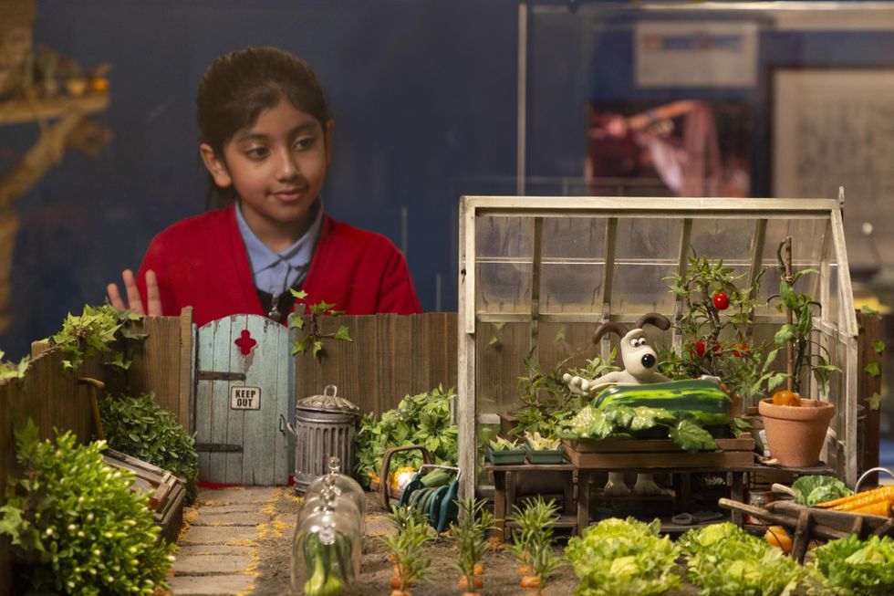 Girl admires a Gromit diorama with greenhouse and garden vegetables.