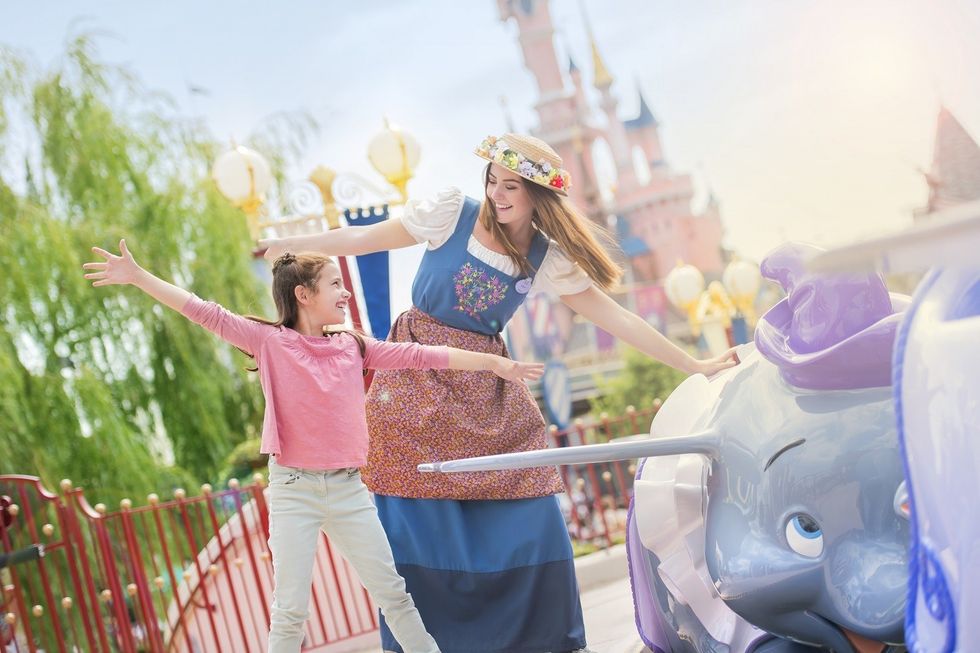 Girl and woman joyfully posing near Dumbo ride in a Disney theme park.
