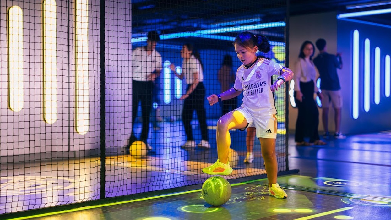Girl in soccer jersey plays with a ball indoors, surrounded by neon lights.