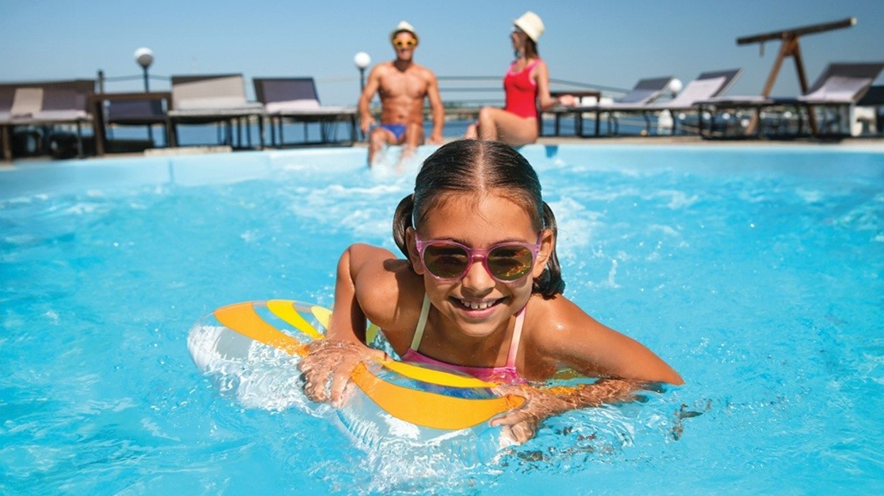 Girl in sunglasses swimming with float in a pool; adults relaxing in background.