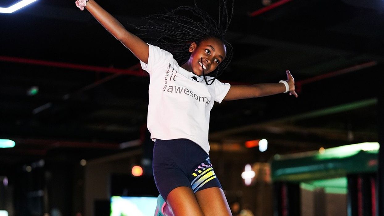 Girl jumping joyfully indoors with outstretched arms, wearing a white shirt and shorts.
