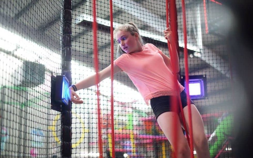 Girl touches wristband to TAG Active touchpoint on ropes course from iplayco showcasing at Amuseument Expo 2020