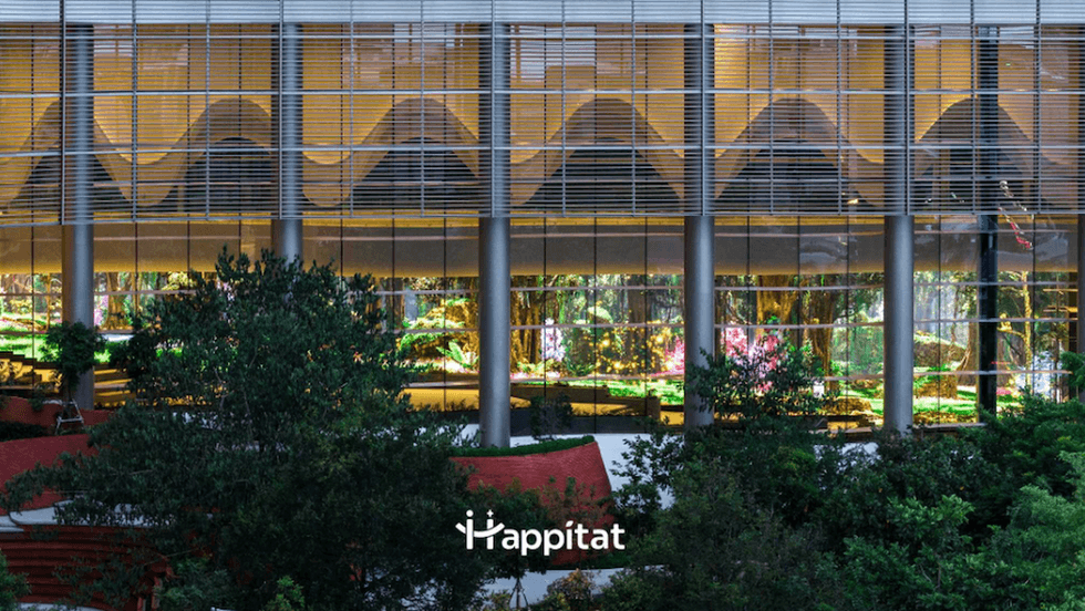 Glass building facade with lit geometric patterns, surrounded by lush greenery.