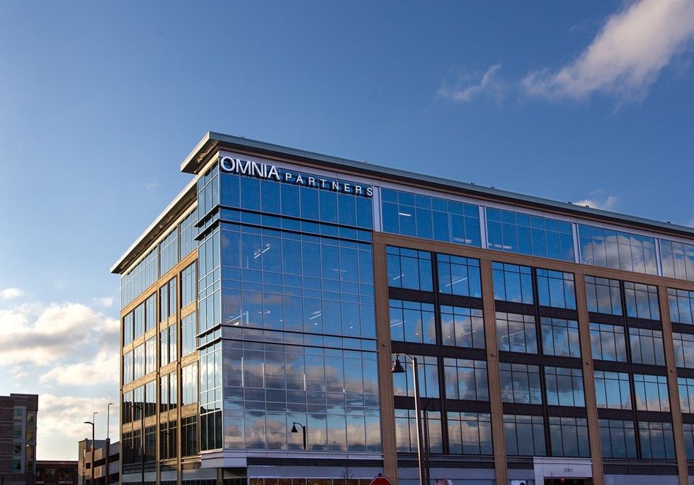 Glass office building with "OMNIA PARTNERS" sign against a blue sky.