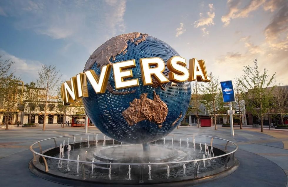 Globe fountain with "Universal" letters in a theme park, surrounded by trees.