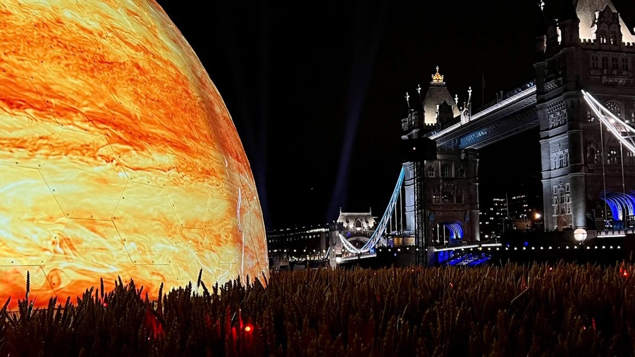 Glowing giant sphere beside Tower Bridge at night, set against a field of wheat.