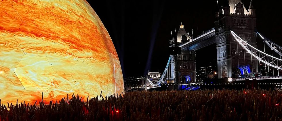 Glowing giant sphere beside Tower Bridge at night, set against a field of wheat.