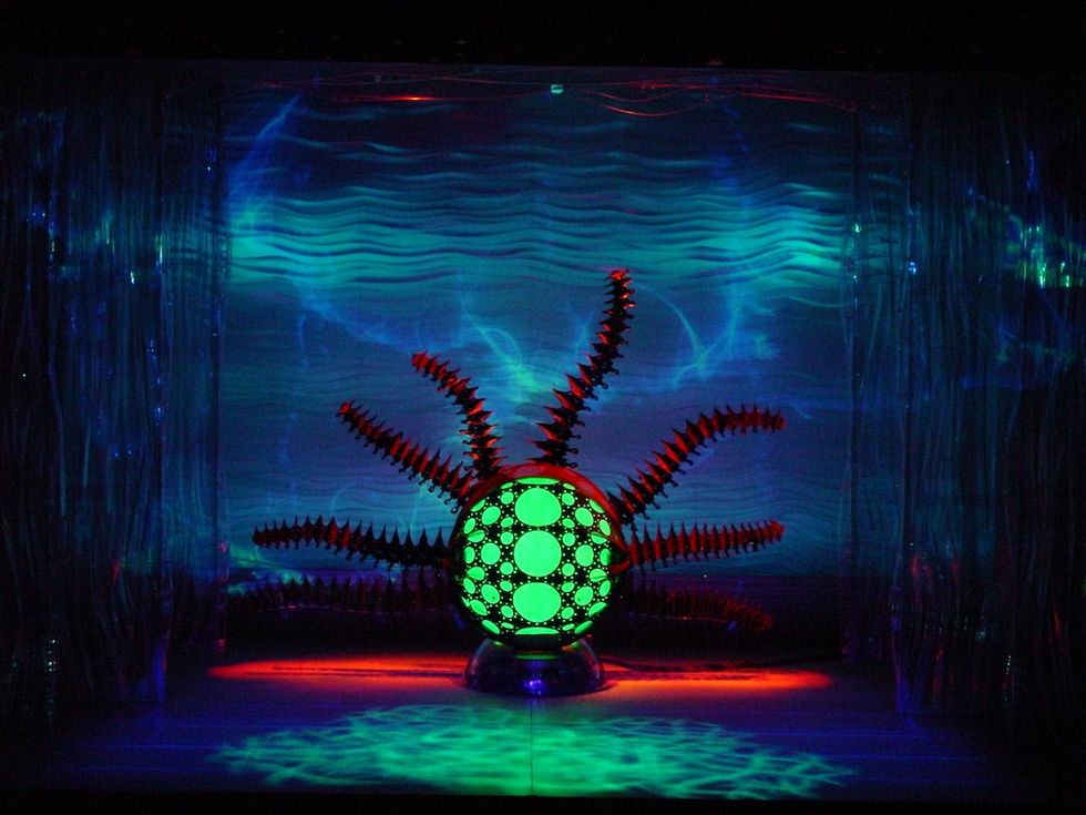 Glowing green sci-fi structure with red spikes in a dark, wavy blue-lit setting.